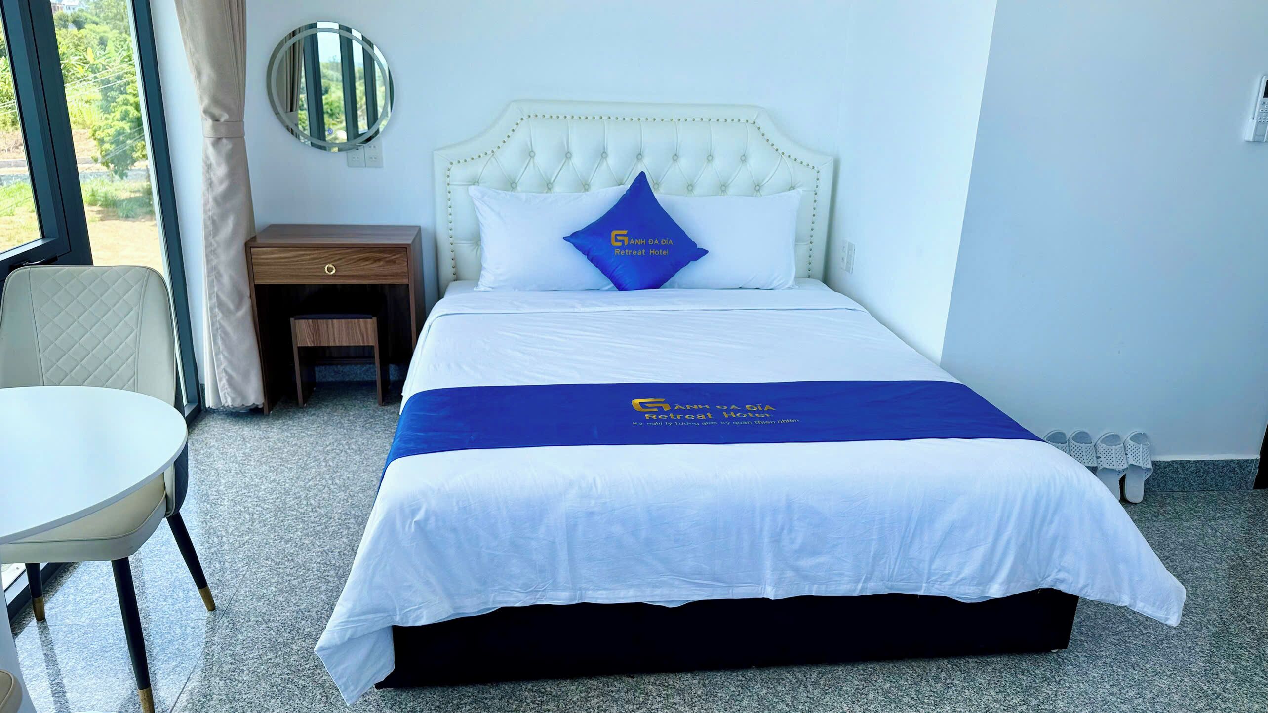 Una habitación de hotel con una cama, una mesita, una silla, una mesita de noche y un espejo.