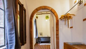 Un baño con un arco de ladrillo, una bañera, un tocador de madera y una planta colgante.