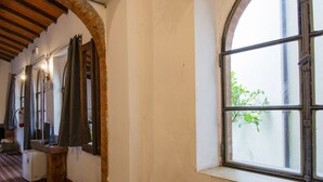 Un pasillo con suelo de baldosas, techo de madera y una ventana que ofrece vistas a follaje exterior.
