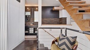 A modern interior with a wooden staircase, a kitchen area, and a seating area with a chair and cushion. - Vital Urban: Spa Inspired Retreat (Chicago)