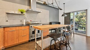 A modern kitchen with a central island, stainless steel appliances, and a large window offering a view of the outdoors. - Vital Urban: Spa Inspired Retreat (Chicago)