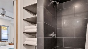 A modern bathroom with a shower, dark tiles, and a towel rack. - Vital Urban: Spa Inspired Retreat (Chicago)