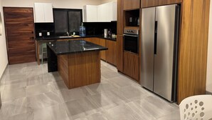 Una cocina moderna con una isla central, armarios de madera, electrodomésticos de acero inoxidable y un piso de baldosas de color claro.