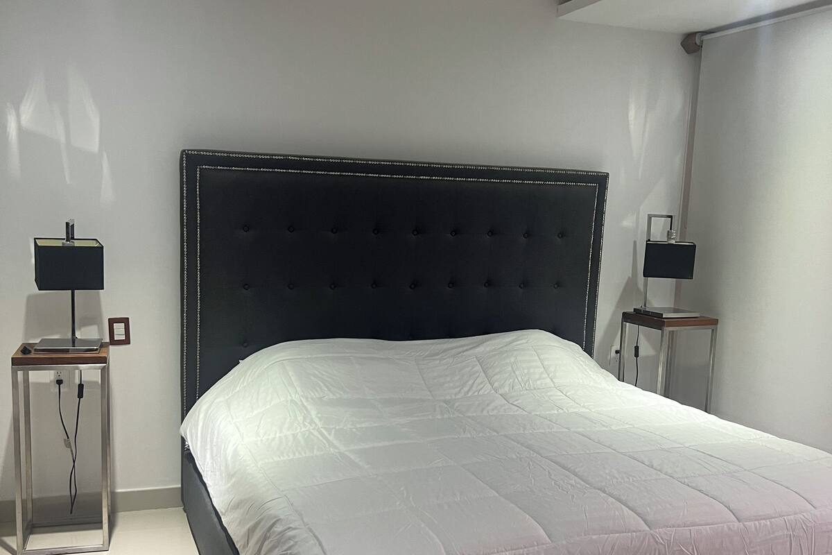 A modern bedroom with a large bed, two bedside tables with lamps, a ceiling fan, and recessed lighting.