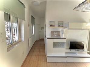 Una sala de estar moderna con un televisor de pantalla plana, un mueble blanco para el equipo de sonido y una ventana con persianas.