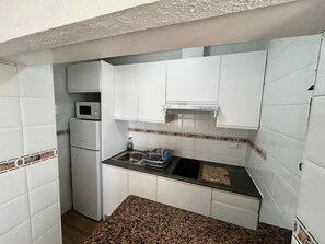 Uma cozinha compacta com armários brancos, micro-ondas, pia e um pequeno balcão.