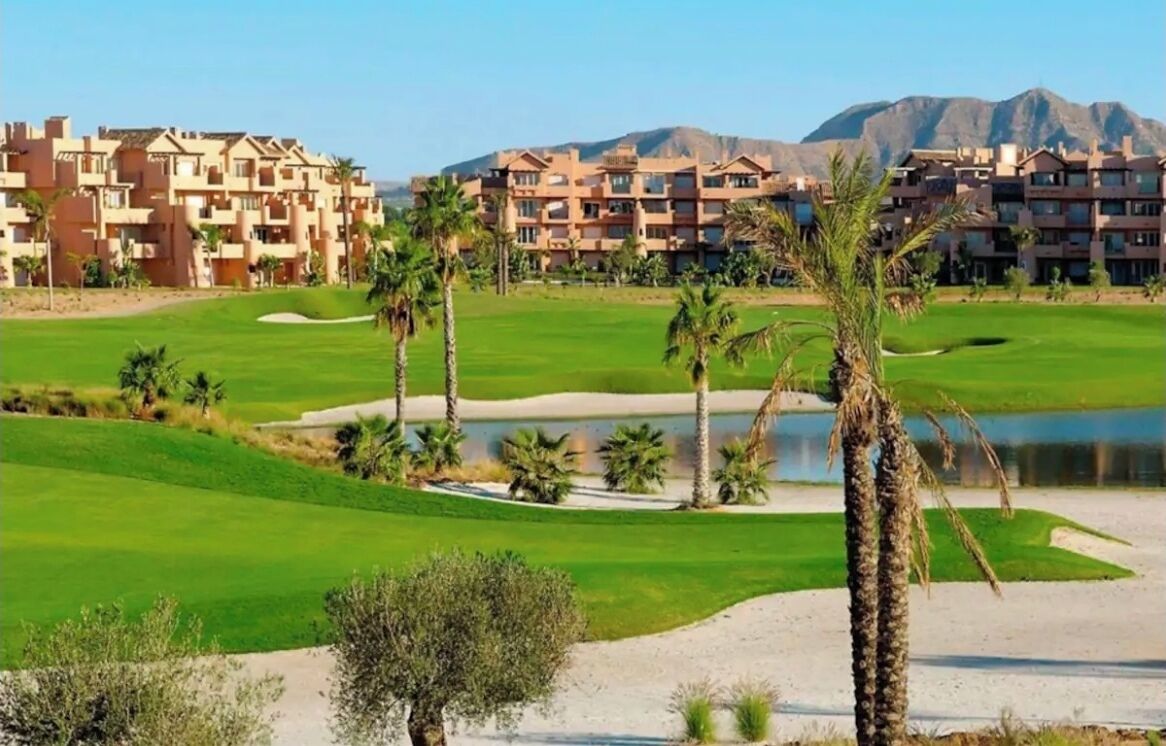 Un parcours de golf agrémenté d’un obstacle d’eau, de palmiers et dominé par un paysage montagneux.