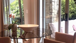 A modern dining area with a glass table and chairs, a large mirror, and a view of greenery outside.