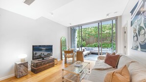 A modern living room with a large TV, wooden flooring, a glass coffee table, and a sofa with cushions.