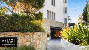 A stone wall with a sign reading "AMARI 38 OCEAN STREET (NITH)" leading to a modern building with a glass entrance.