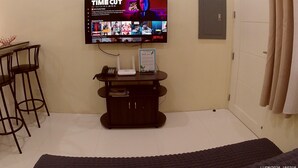 A room with a mounted TV displaying a movie, a desk with a phone and a sign, and a door with a curtain. - Entire home/Fully furnished/Netflix/AC/Wash/Dyer (Daet)