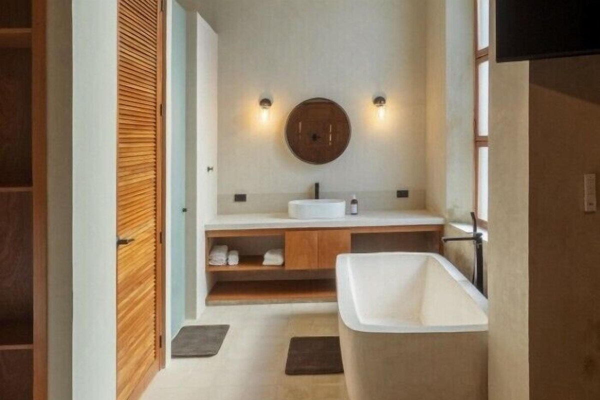 Ein modernes Badezimmer mit einer freistehenden Badewanne, einem Holzwaschtisch und einem runden Spiegel.