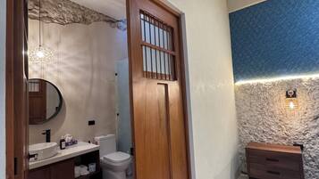 Un baño con puerta de madera, espejo redondo, lavamanos e inodoro.