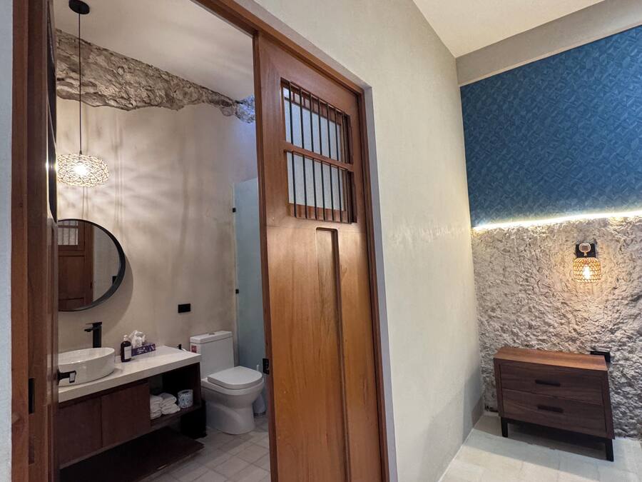 Un baño con puerta de madera, espejo redondo, lavamanos e inodoro.
