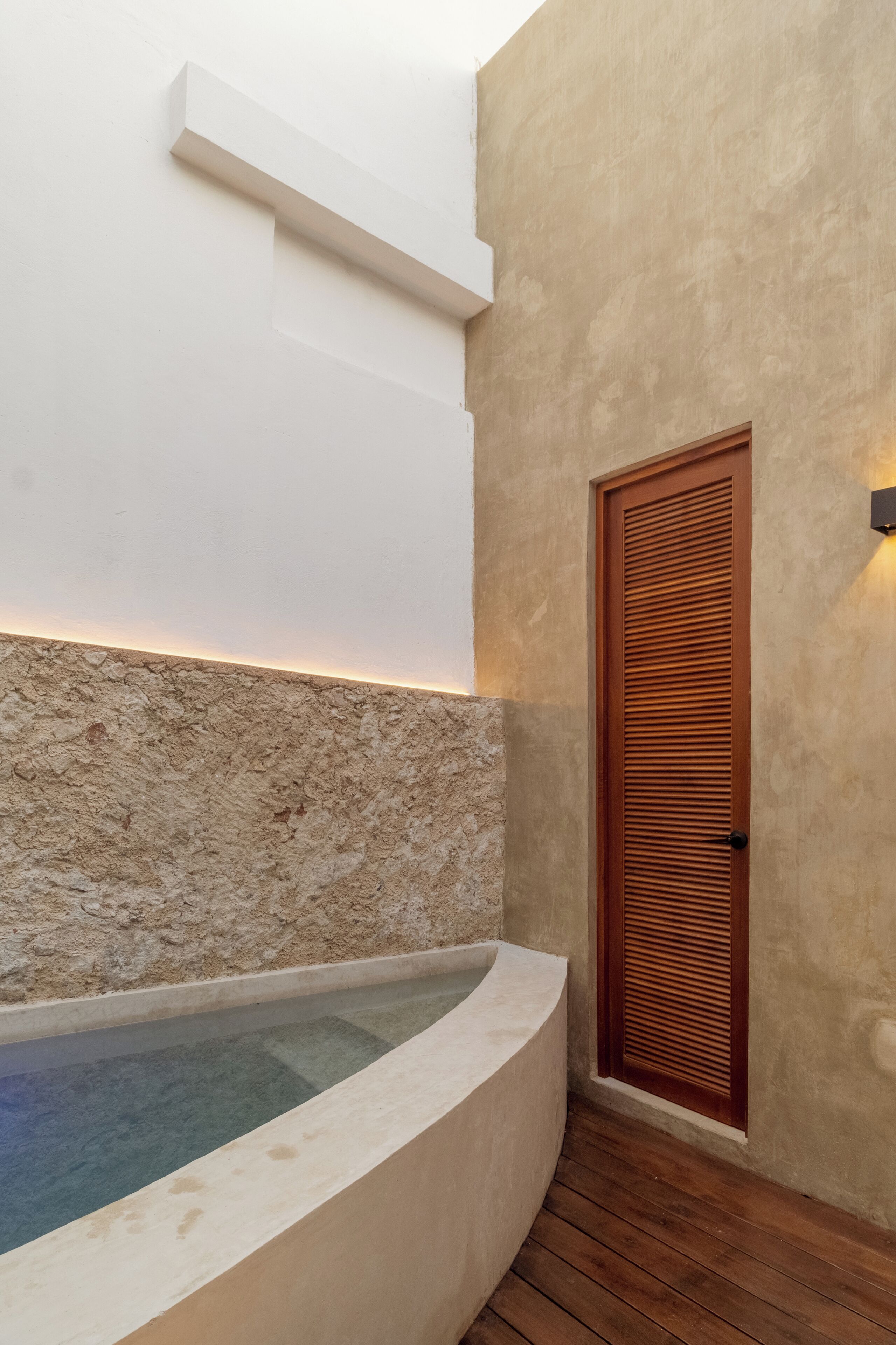 Un espace spa agrémenté d’un mur en pierre, d’une porte en bois et d’un jacuzzi encastré.