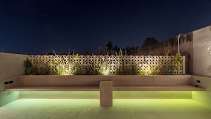 A rooftop terrace with a geometric patterned wall, a central stone bench, and a low wall with plants. - Casa Tunkul (Mérida)