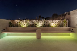 Eine Dachterrasse mit einer Wand im geometrischen Muster, einer zentralen Steinsitzbank und einer niedrigen Mauer mit Pflanzen.