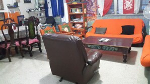 Una sala de estar con un sofá de cuero marrón, un sofá naranja, una mesa de comedor de madera con sillas y una estantería.