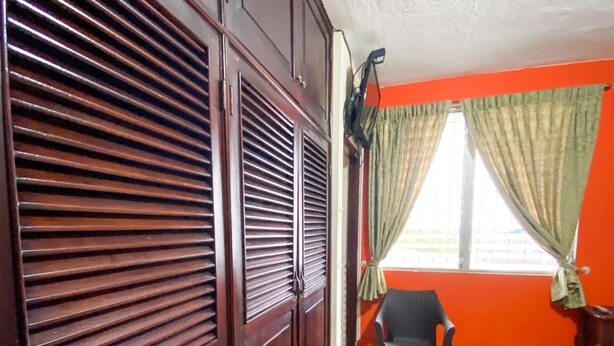 Una habitación con armario de madera, una silla, una cama y una ventana con cortinas.