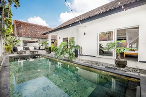 Ein modernes Haus mit Swimmingpool, Sitzgelegenheiten im Freien und Topfpflanzen.