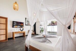 Ein Schlafzimmer mit einem Himmelsbett, einer hölzernen Bank, einem an der Wand befestigten Fernseher und Blick ins Freie.