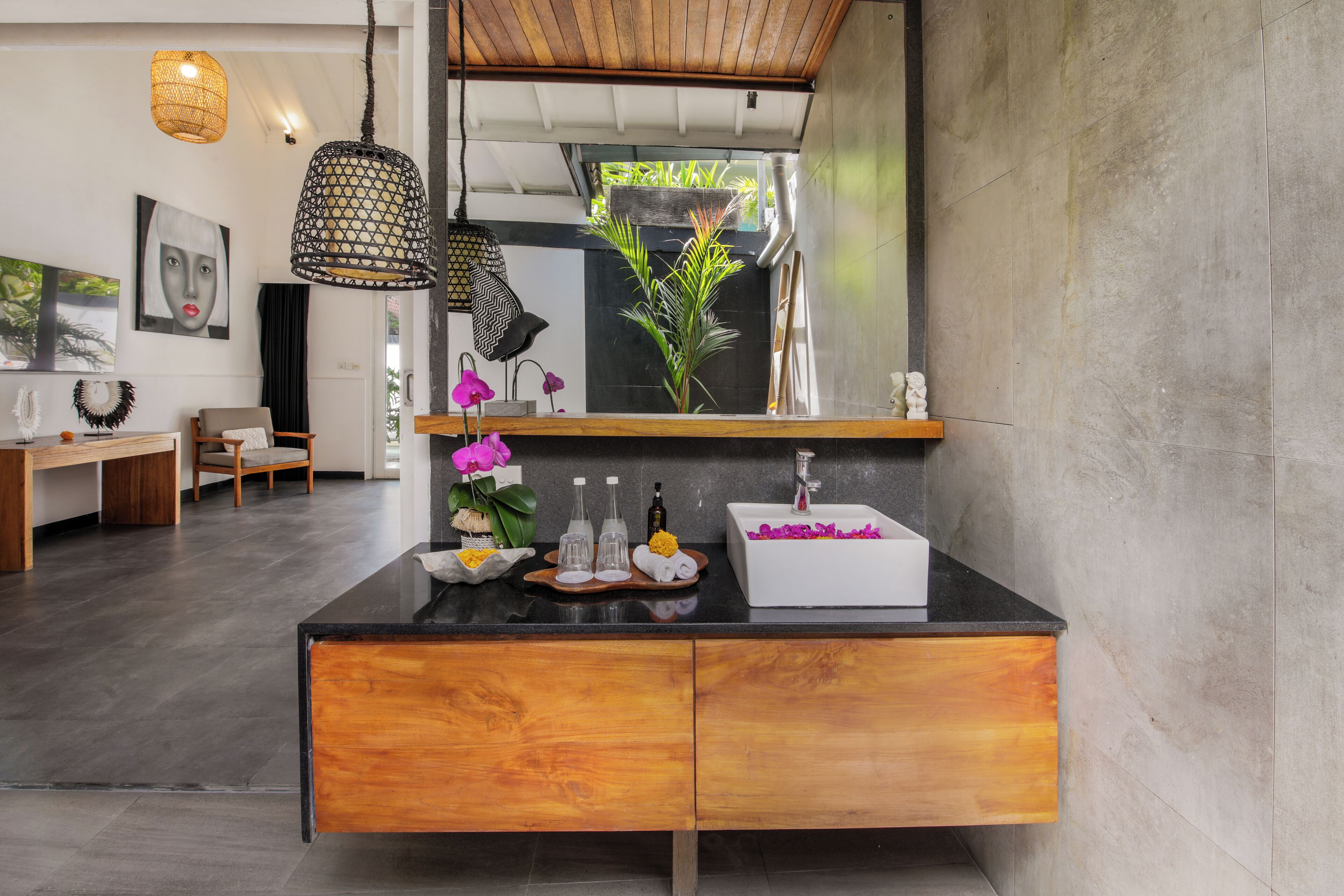A modern bathroom with a black countertop, wooden cabinets, a large mirror, and a potted plant.