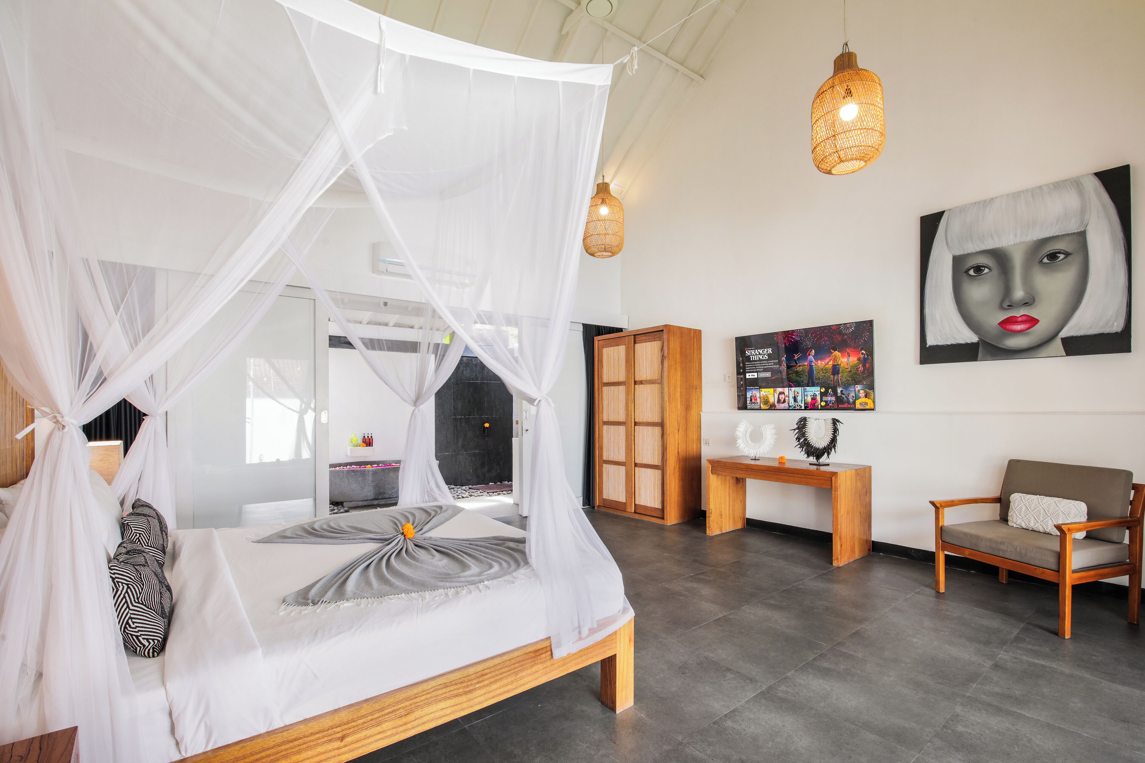 A bedroom with a four-poster bed, a wooden nightstand, a chair, and artwork on the wall.