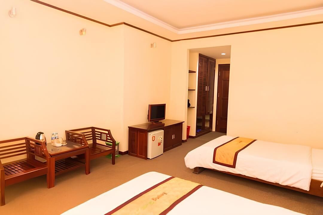 A hotel room with a bed, a desk with a chair, a television, a small refrigerator, and a wardrobe.