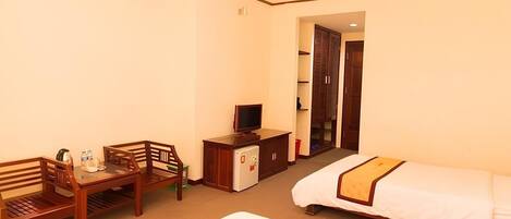Habitación de hotel con cama, escritorio con silla, televisor, refrigerador pequeño y armario.