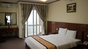 A hotel room with a large bed, a desk with a chair, a mirror, and a window with curtains. - Bac Kinh Hotel Vinh - by BAY LUXURY (Vinh Phu)