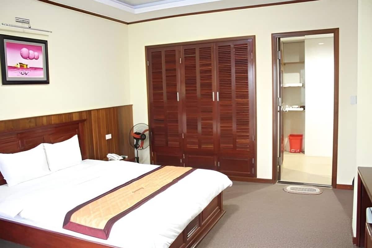 A hotel room with a large bed, wooden wardrobe, and a door leading to a bathroom.