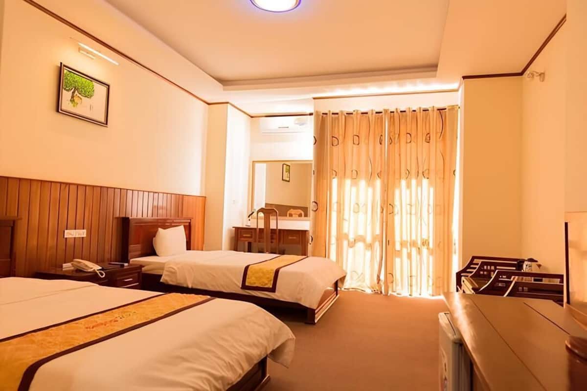 A hotel room with two beds, a wooden headboard, a desk, a mirror, and a window with curtains.