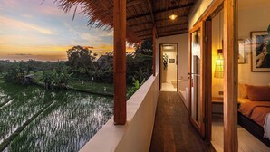 A wooden balcony with a view of a rice field at sunset.