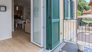 Een balkon met een schuifdeur, een eethoek met een tafel en stoelen, en uitzicht op een woonstraat.
