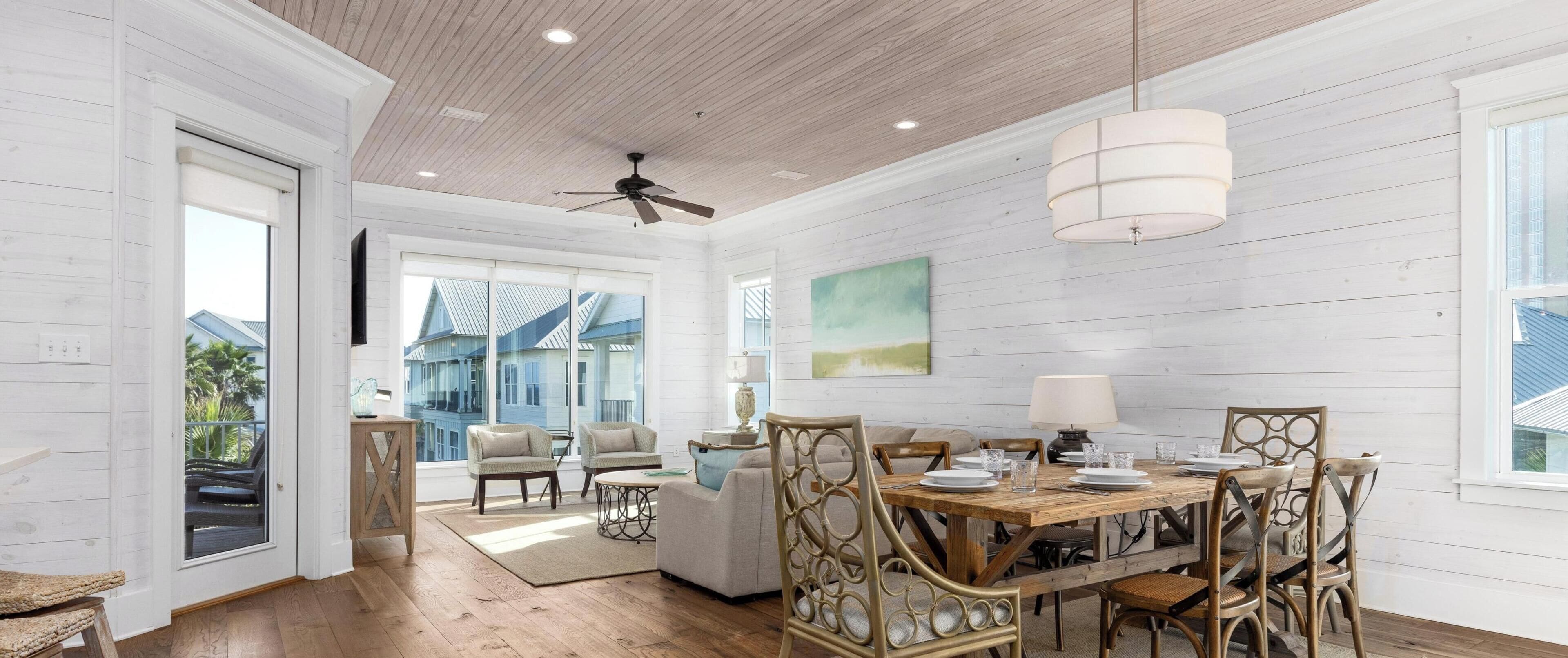 A spacious living room with a wooden floor, a dining area with a wooden table and chairs, and a ceiling fan.