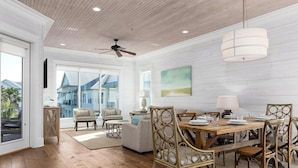 A spacious living room with a wooden floor, a dining area with a wooden table and chairs, and a ceiling fan. - Sea You Later by Kaiser Vacation Rentals Cottages at Romar 15 (Orange Beach)