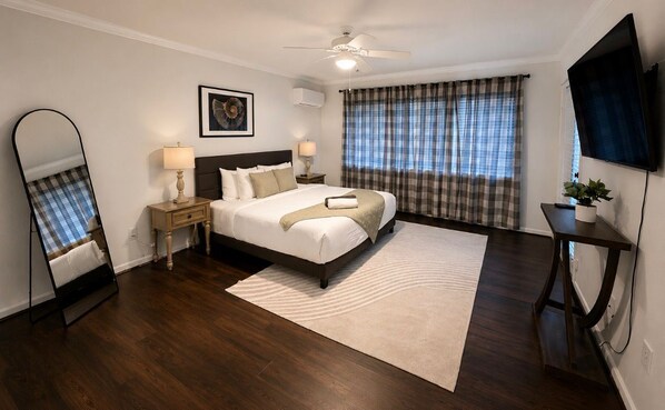 A bedroom with a bed, a ceiling fan, a TV, a large window with curtains, a bedside table with a lamp, and a mirror. - Modern Houston Home nr Med Center & NRG - Pool, Wi‑Fi, Parking, Family‑Friendly (Houston)