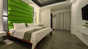 A modern bedroom with a green upholstered headboard, a bed with white bedding, a bedside table, a wall-mounted TV, and a ceiling light fixture. - Dream'Star Resort Puerto Galera powered by Cocotel (Puerto Galera)