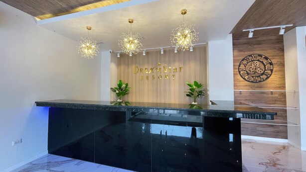 A reception area with a black marble counter, modern chandeliers, a wooden wall with a clock, and two potted plants. - Dream'Star Resort Puerto Galera powered by Cocotel (Puerto Galera)