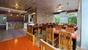 A spacious dining area with wooden tables and chairs, a stone wall, and a large window providing a view of greenery. - Dream'Star Resort Puerto Galera powered by Cocotel (Puerto Galera)