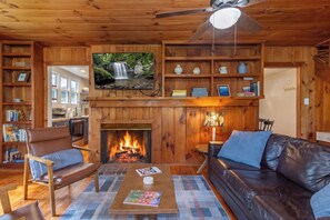 A cozy living room with a fireplace, wooden shelves, a television, and leather furniture.