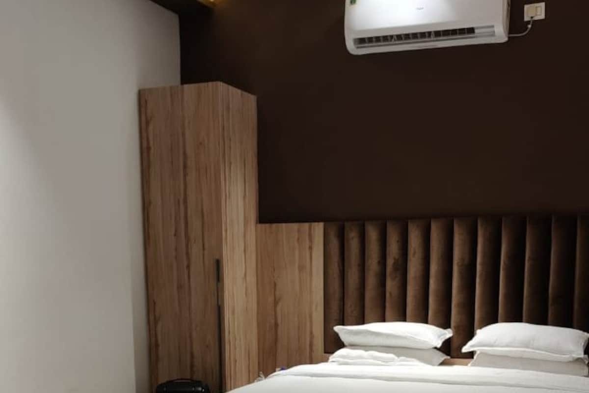 A modern bedroom with a bed, a chair, a wardrobe, and an air conditioning unit.