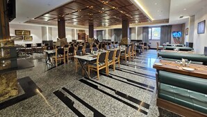Een ruime hotel eetruimte met meerdere tafels en zitjes, een gepolijste granieten vloer en een modern plafondontwerp.
