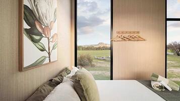A bedroom with a large window, a bed with green bedding, a painting of flowers, and a wooden shelf with hangers.