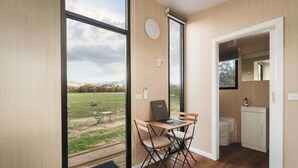 A modern room with a large window, a laptop on a wooden table, and a compact kitchenette. - Hollow Mountain Getaway 1 by Tiny Away (Laharum)