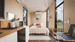 A modern bedroom with a bed, bedside table, and a view of the outdoors.
