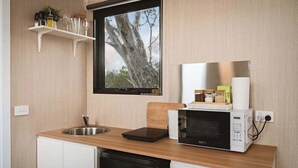 A compact kitchen with a sink, a microwave, and a window with a view of trees.