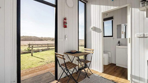 A room with a wooden table and chairs, a fire extinguisher, a window, and a view of the outdoors. - Rosebrook Riverviews by Tiny Away (Rosebrook)