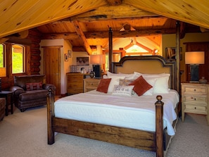Ein Schlafzimmer in einer Blockhütte mit einem großen Bett, einem Holzkopfende und einem gemütlichen Kamin.