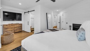 A modern bedroom with a large bed, a ceiling fan, a TV, and a fireplace.